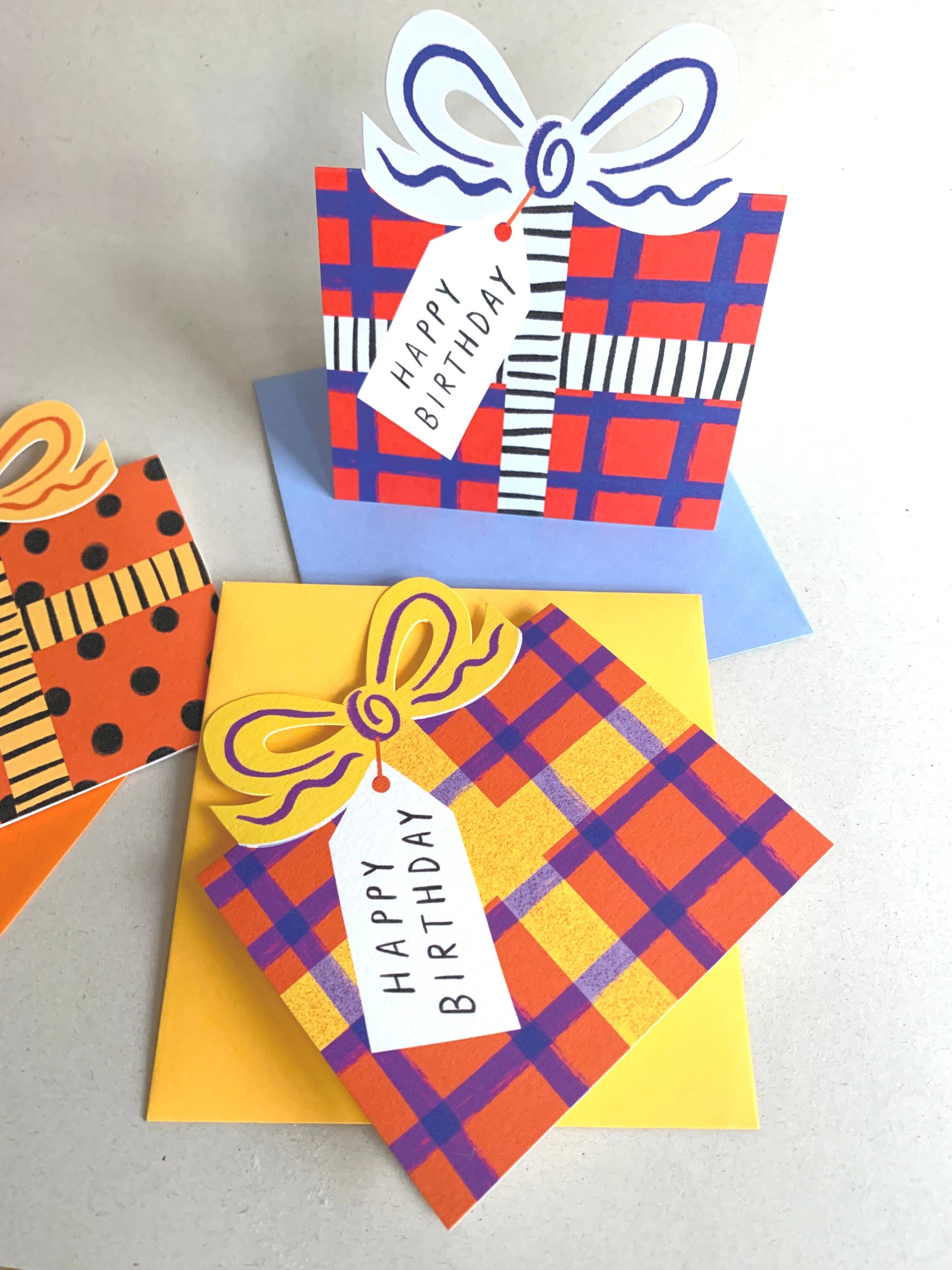 Colorful birthday cards with plaid patterns and 'Happy Birthday' tags on a light gray background.