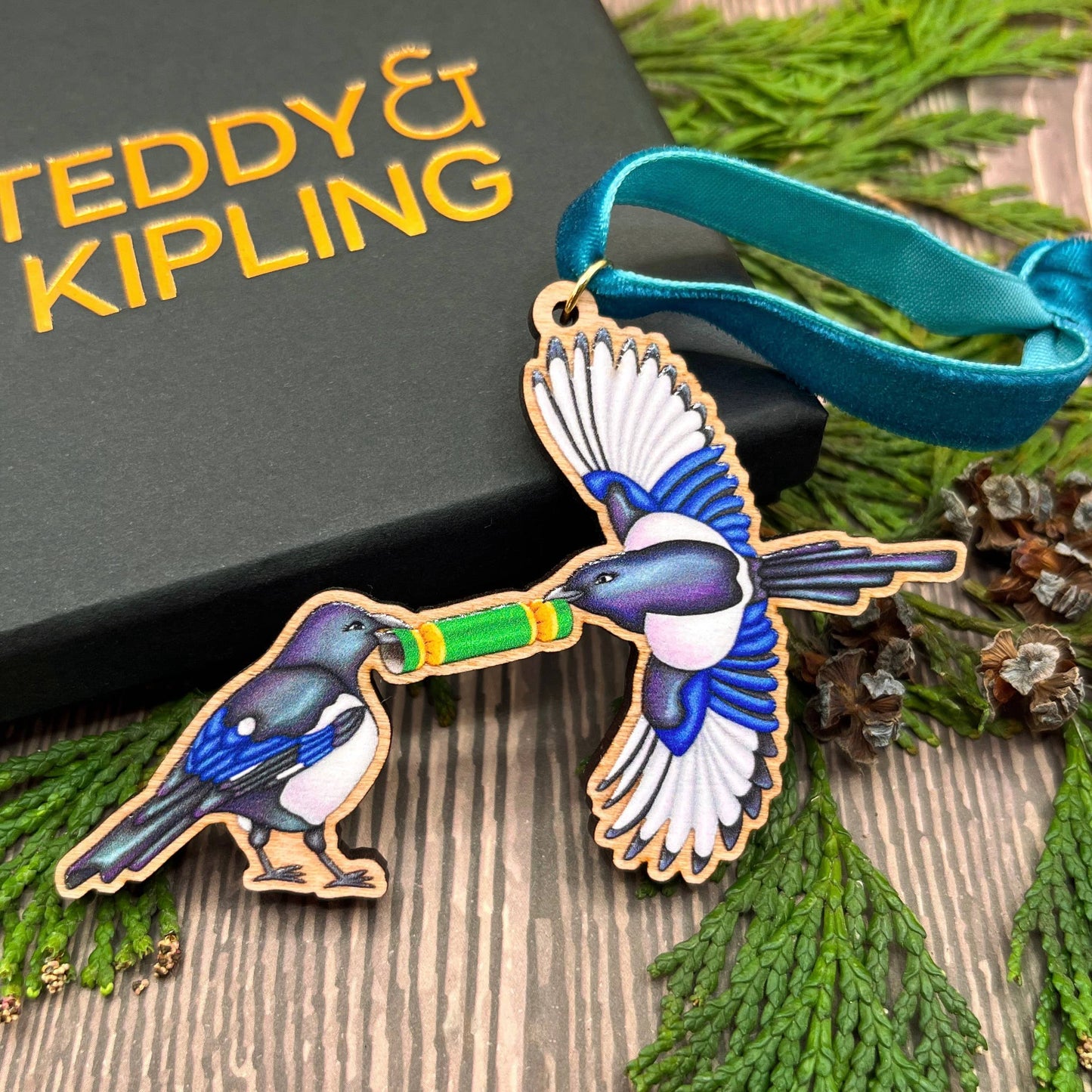 Magpie wooden Christmas tree decoration featuring Teddy & Kipling illustration, sustainably certified cherry wood, gold-plated ring, and dark teal velvet ribbon