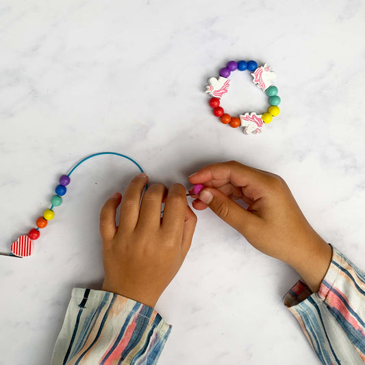 Child's hand threading wooden beads onto elastic from the bracelet making kit