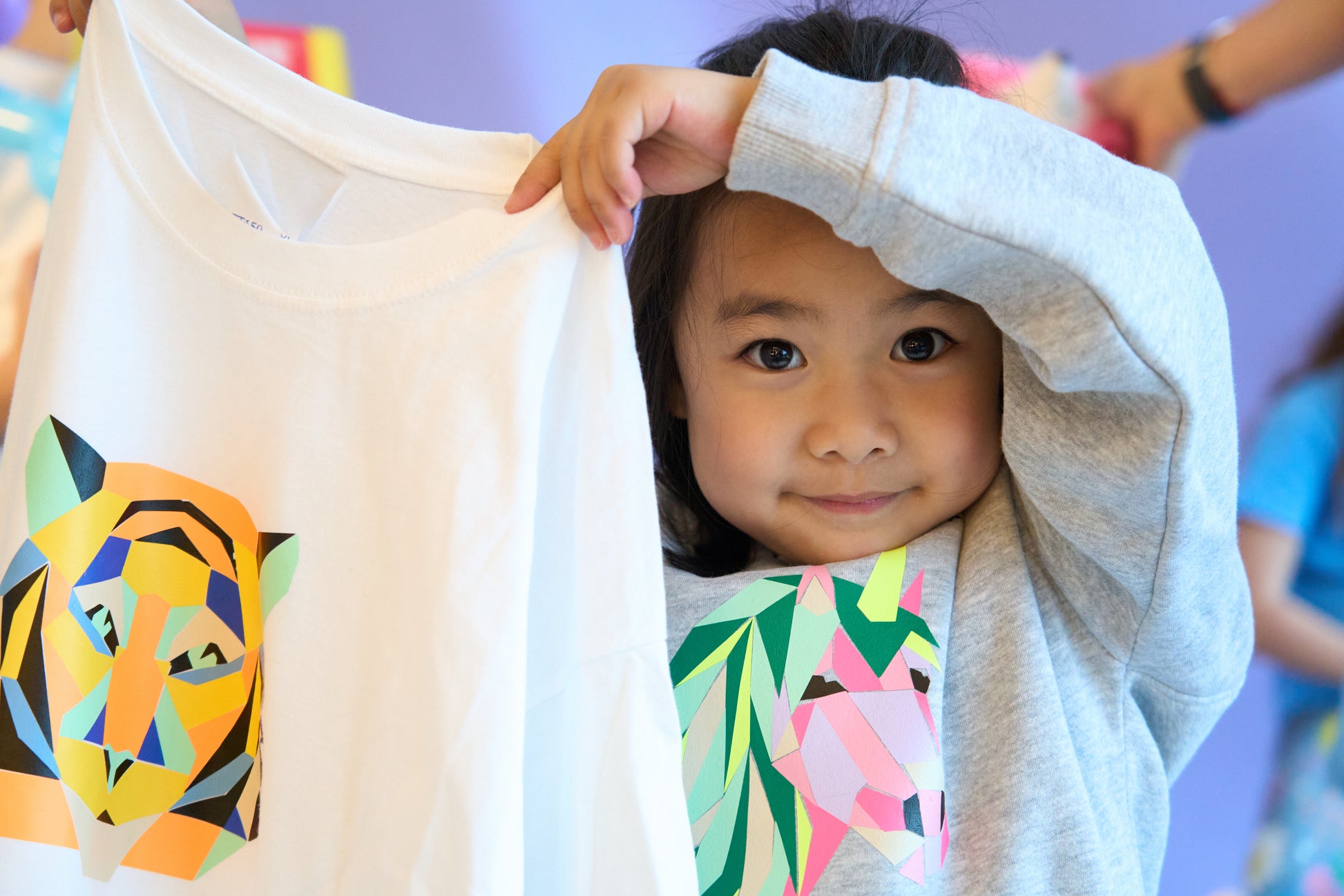 A little smiling girl, holding up her creation of  Tiger Pop Kit ironed on to a white sweater.