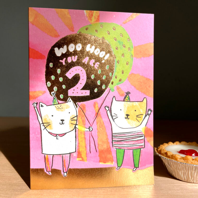 Children's birthday card with two cats holding balloons on a pink background. Two Today Gold Foil Balloon 2nd Birthday Card | Laura Skilbeck.