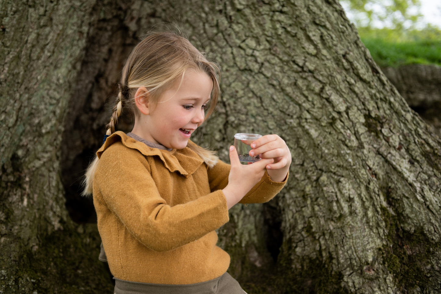 A child looks excitedly at the pot containing an insect.