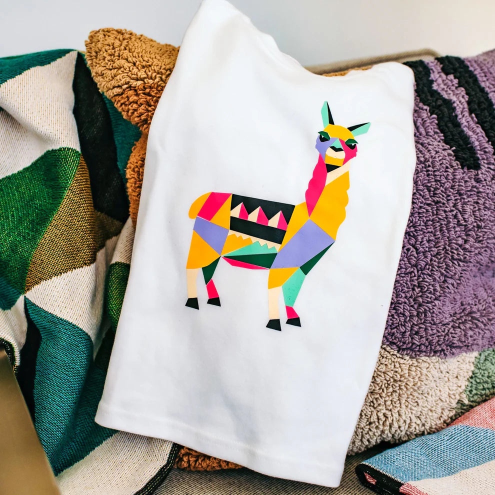 Child's hands applying a colourful llama print from the Popkit Design Studio onto a tote bag.