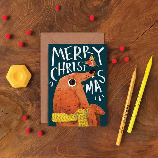 Christmas card with a dog illustration and 'Merry Christmas' text. "Emily Nash Dog & Robin illustrated greeting card with recycled kraft envelope, sustainably certified card