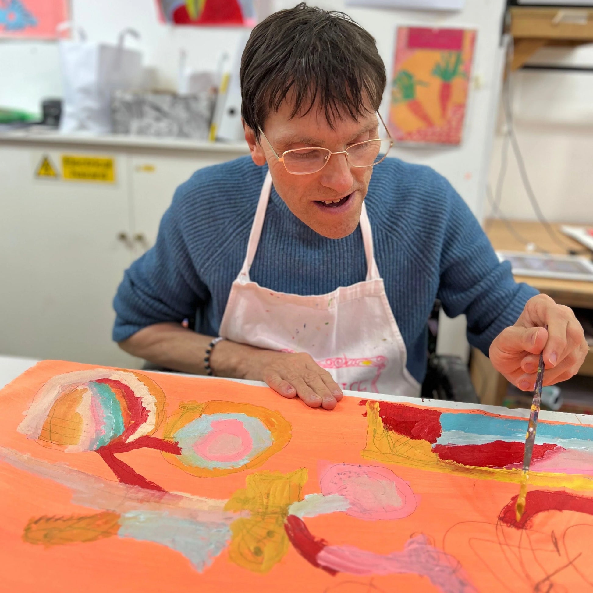 Person in an apron working on a colorful artwork in a studio setting