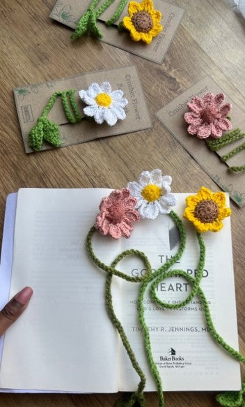 Crocheted flower bookmarks on an open book with a wooden surface background.