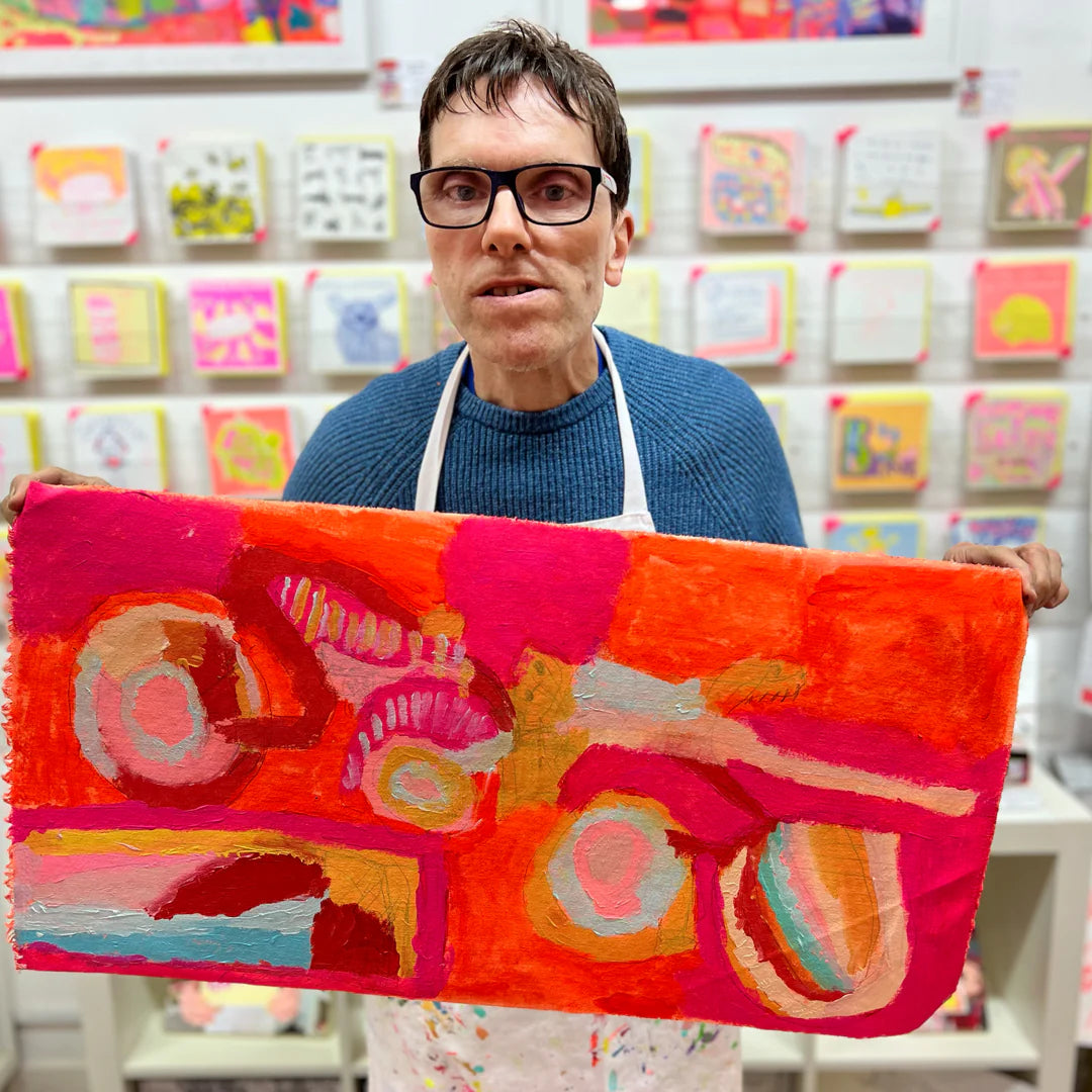 Person holding a colorful abstract artwork in an art studio setting