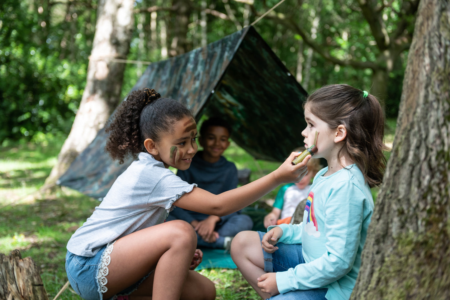 Children having fun face painting with the camouflage face paints next to the erected Den.