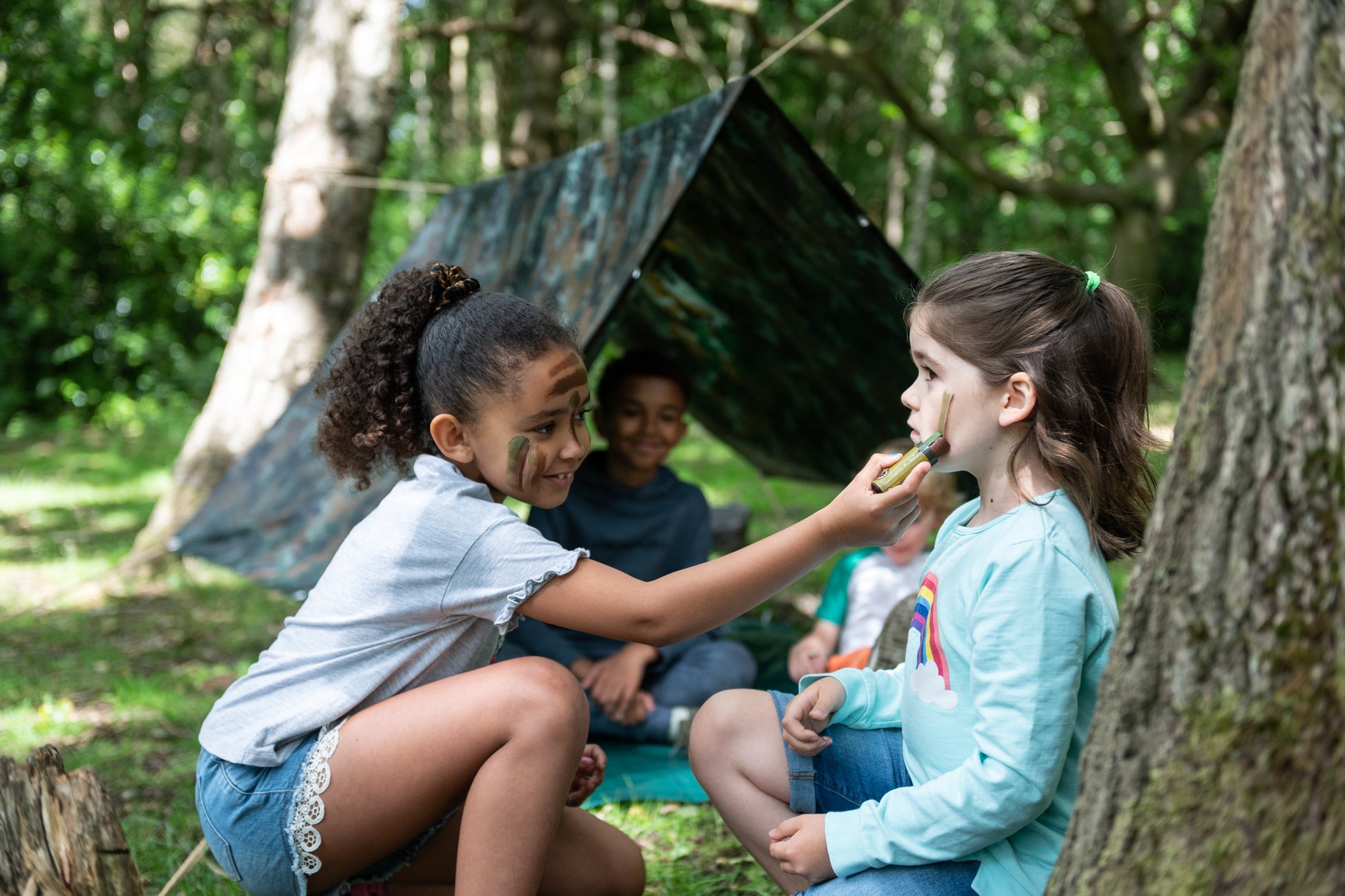Children having fun face painting with the camouflage face paints next to the erected Den.