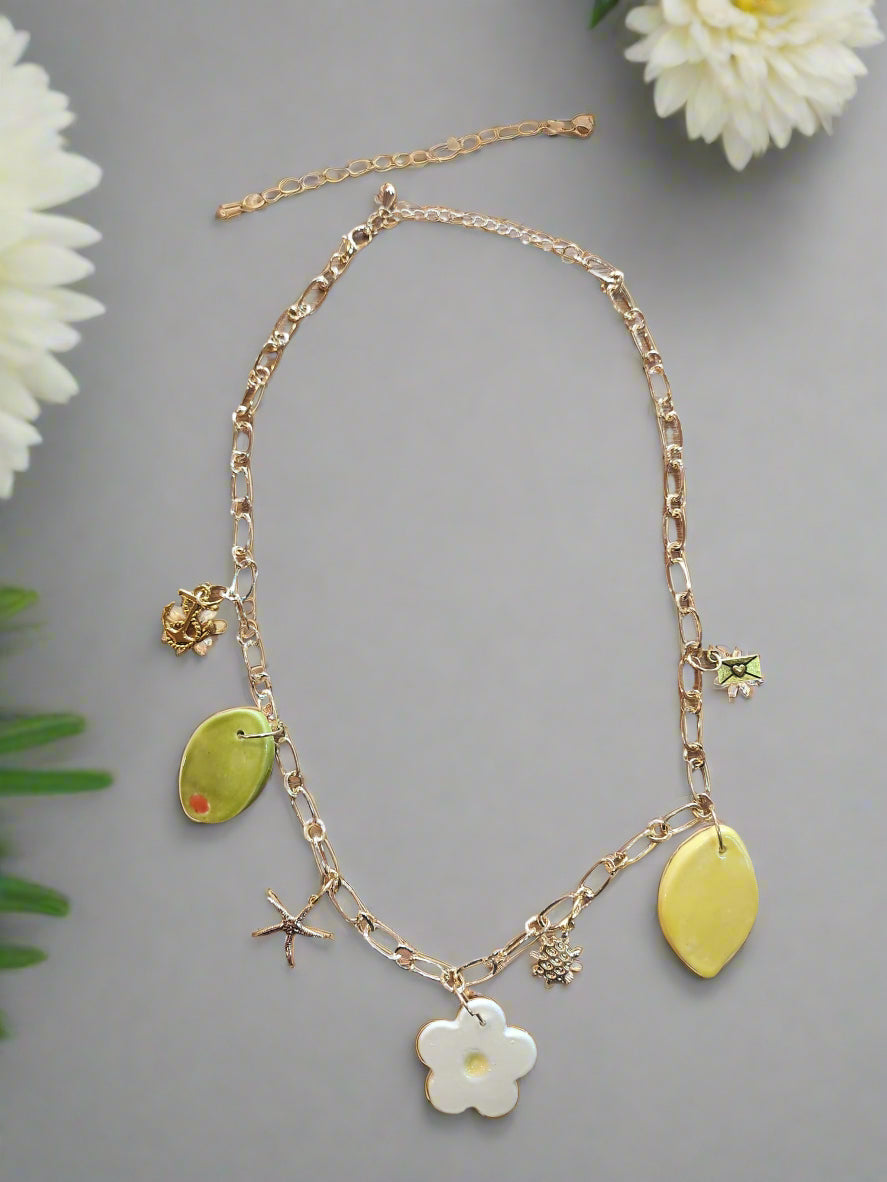 Celebrate Life Chunky Charm Necklace. Lovingly handmade, these ceramic charms are individually cut out from clay slabs and then hand-painted. They are hung on an 18K gold-plated chain. Featuring a ceramic lemon, daisy, olive, and gold charms - starfish, turtle & anchor