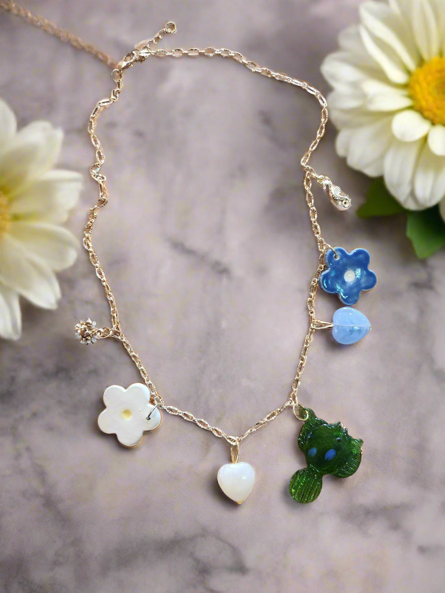 Celebrate Life Chunky Charm Necklace. Lovingly handmade, these ceramic charms are individually cut out from clay slabs and then hand-painted. They are hung on an 18K gold-plated chain. Featuring a ceramic daisy, blue flower, green glass fish, stone hearts in blue and cream, gold charm crab and seahorse