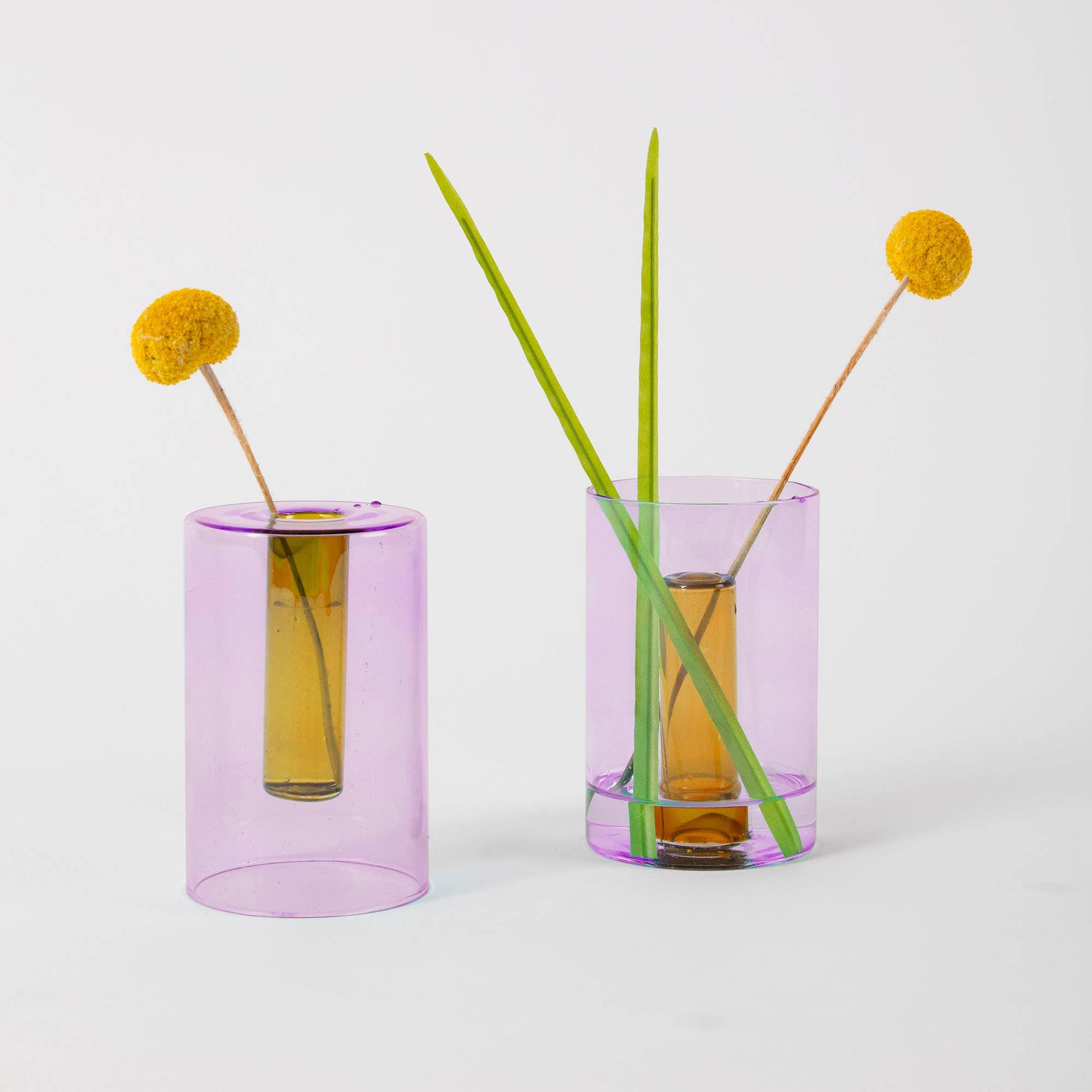 Two purple glass vases with floral arrangements on a light gray background