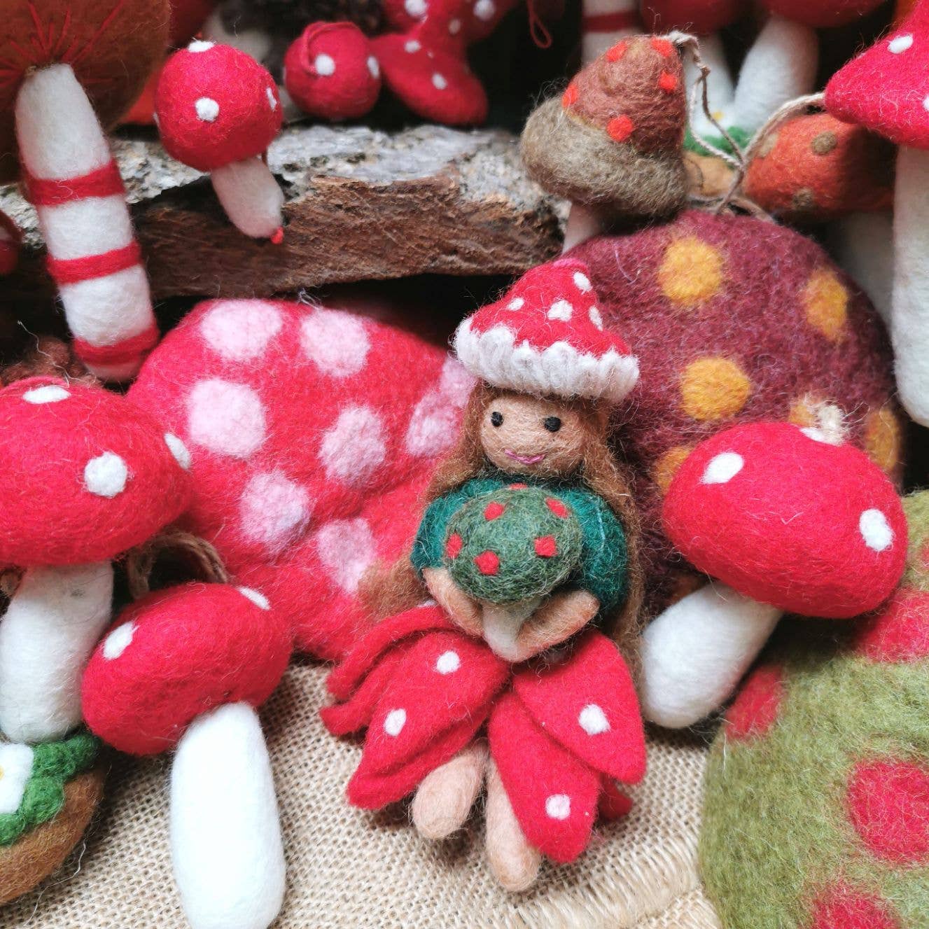 Felted fairy ornament with red mushroom hat and dress on a white background. Handmade felt toadstool fairy autumn hanging decoration with red skirt and hat, sustainable and eco-friendly artisan product. Amongst toadstools.
