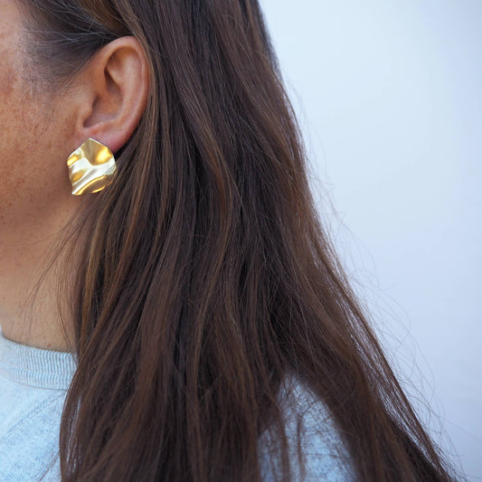 Close up of Purl wavy brass stud earrings with gold tone