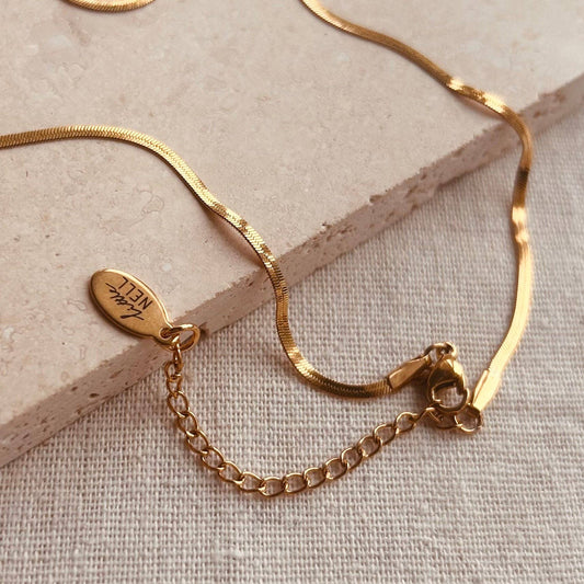 Close-up of the polished gold-plated finish on the Little Nell slim snake chain necklace, highlighting its texture.