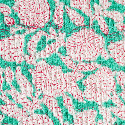 Close-up of a floral pattern with red and green colors on a textured fabric background.