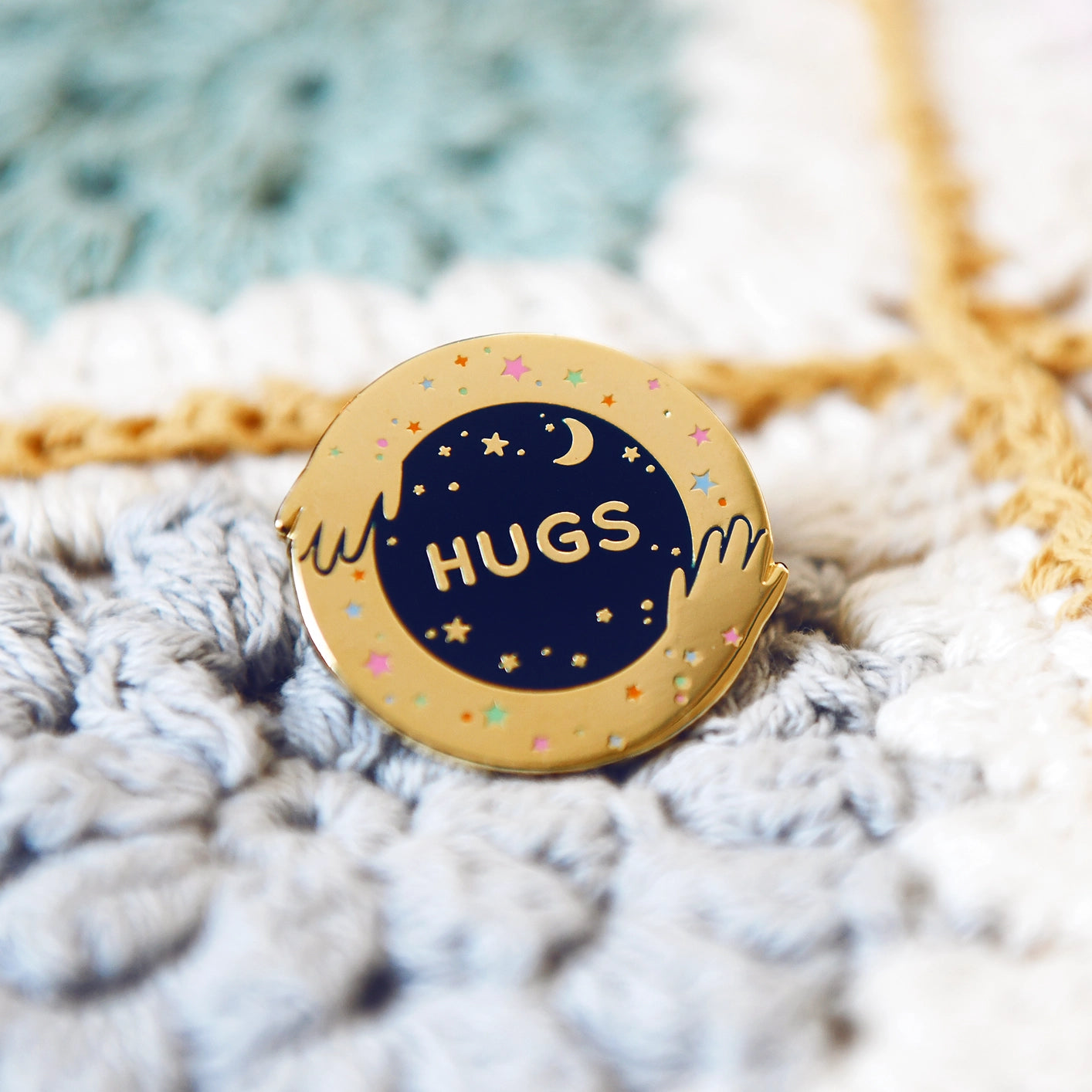 Pin with 'HUGS' text on a textured fabric background