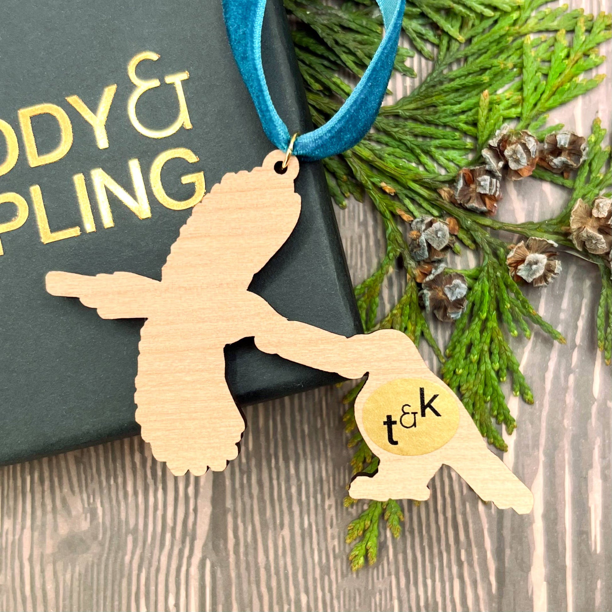 Magpie wooden Christmas tree decoration featuring Teddy & Kipling illustration, sustainably certified cherry wood, gold-plated ring, and dark teal velvet ribbon