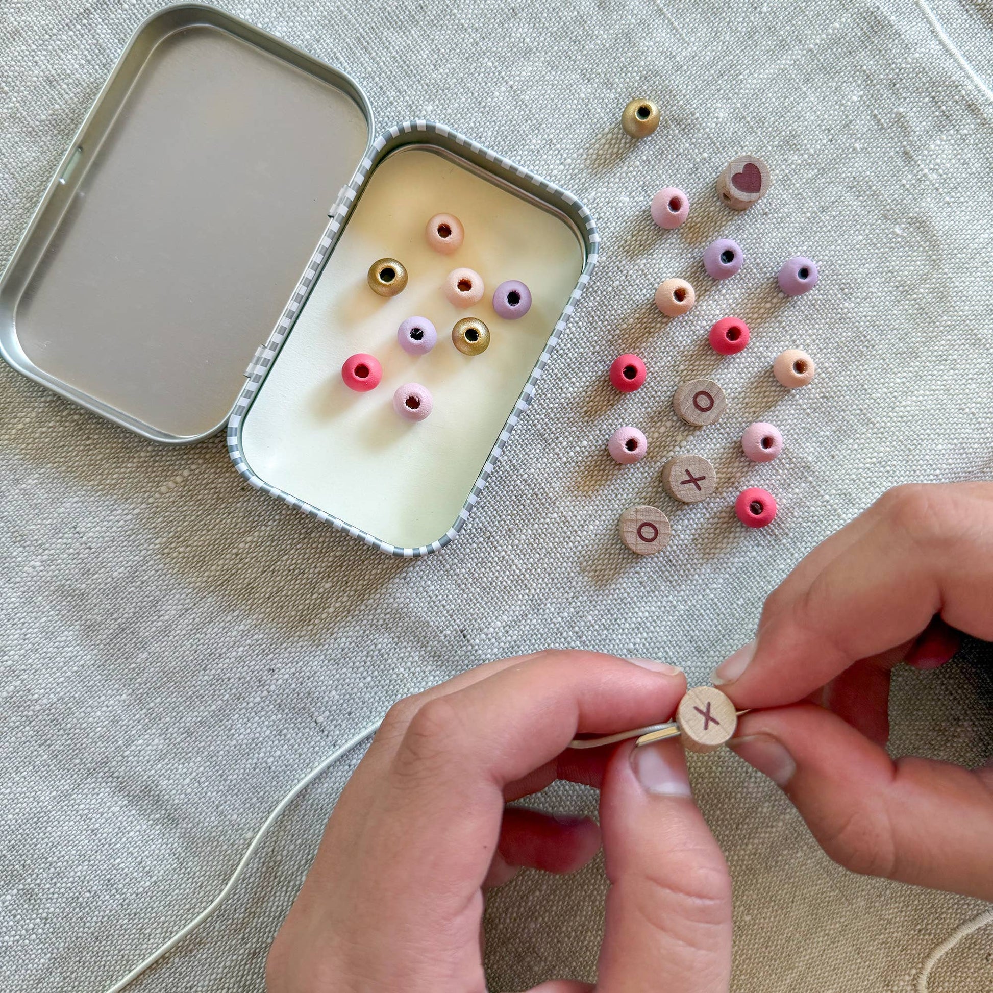 Person assembling small wooden beads with a tin container on a textured surface