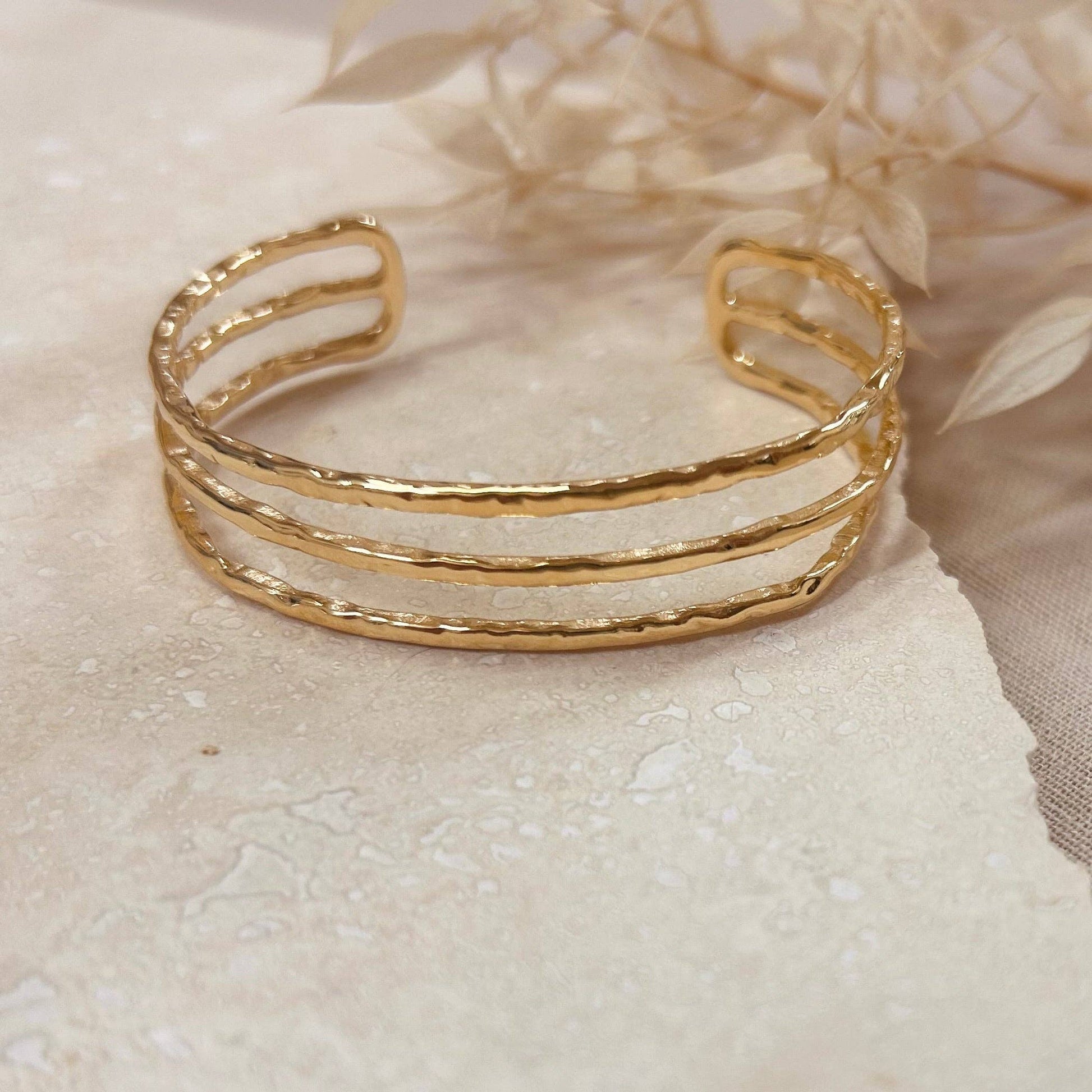 A hammered trio bangle in a polished gold finish. 18k gold plated bracelet. Light and comfortable enough to wear all day, and works well as a stacking piece for a more eye-catching look.
