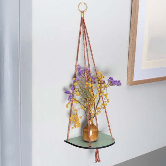 A green wash ‘plant shelf’ that rests neatly against the wall. Colourful twine contrasts nicely with the shelf to make a standout piece. Brass plated hoops and crimp bars finish the look No assembly required. Shown against a white wall, with a small vase of dried flowers.