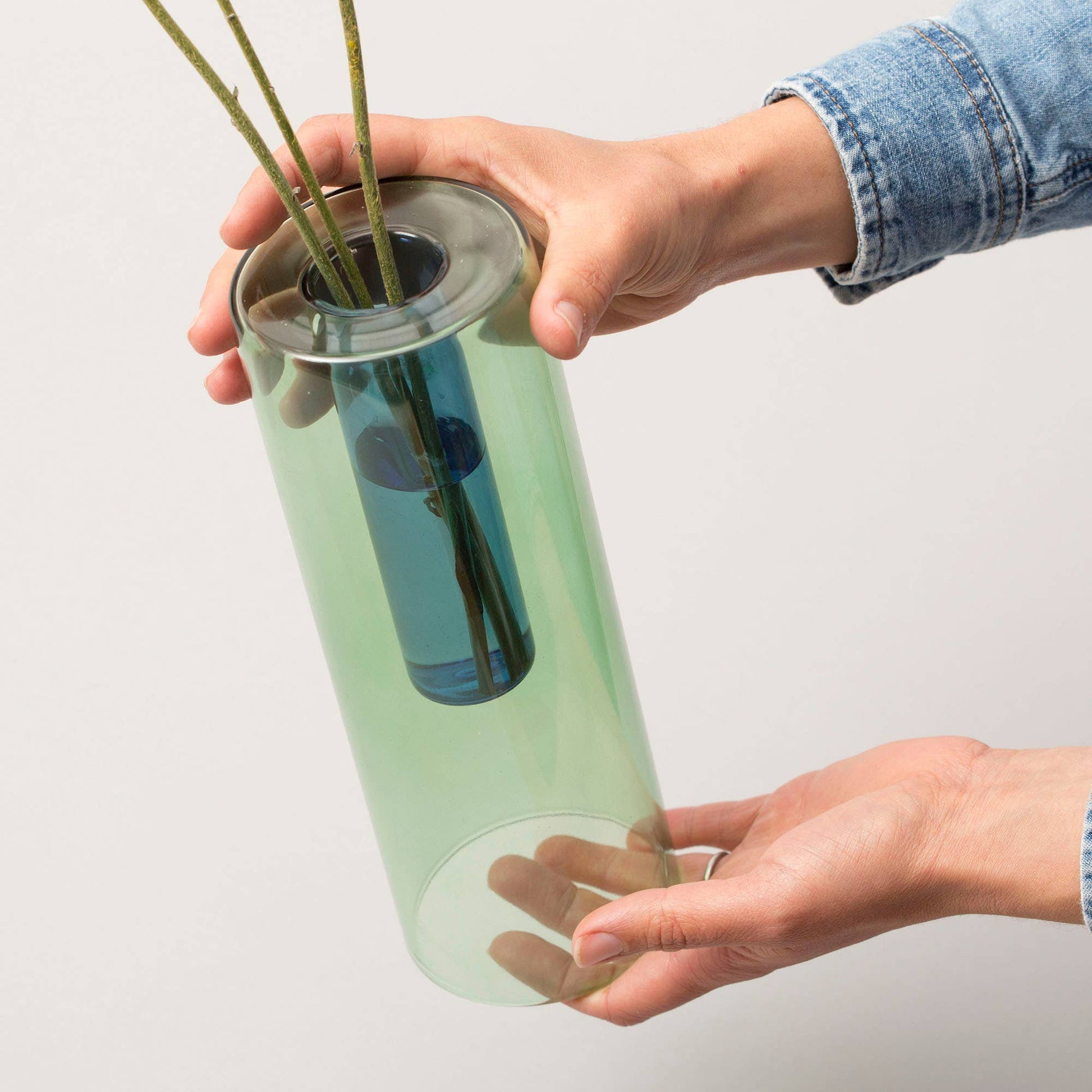 Person holding a cylindrical green vase with a reflective surface against a plain background
