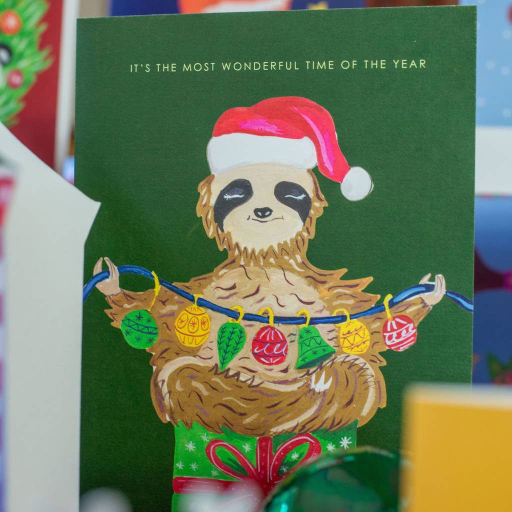 Hand-illustrated Christmas card featuring a sloth on a gift