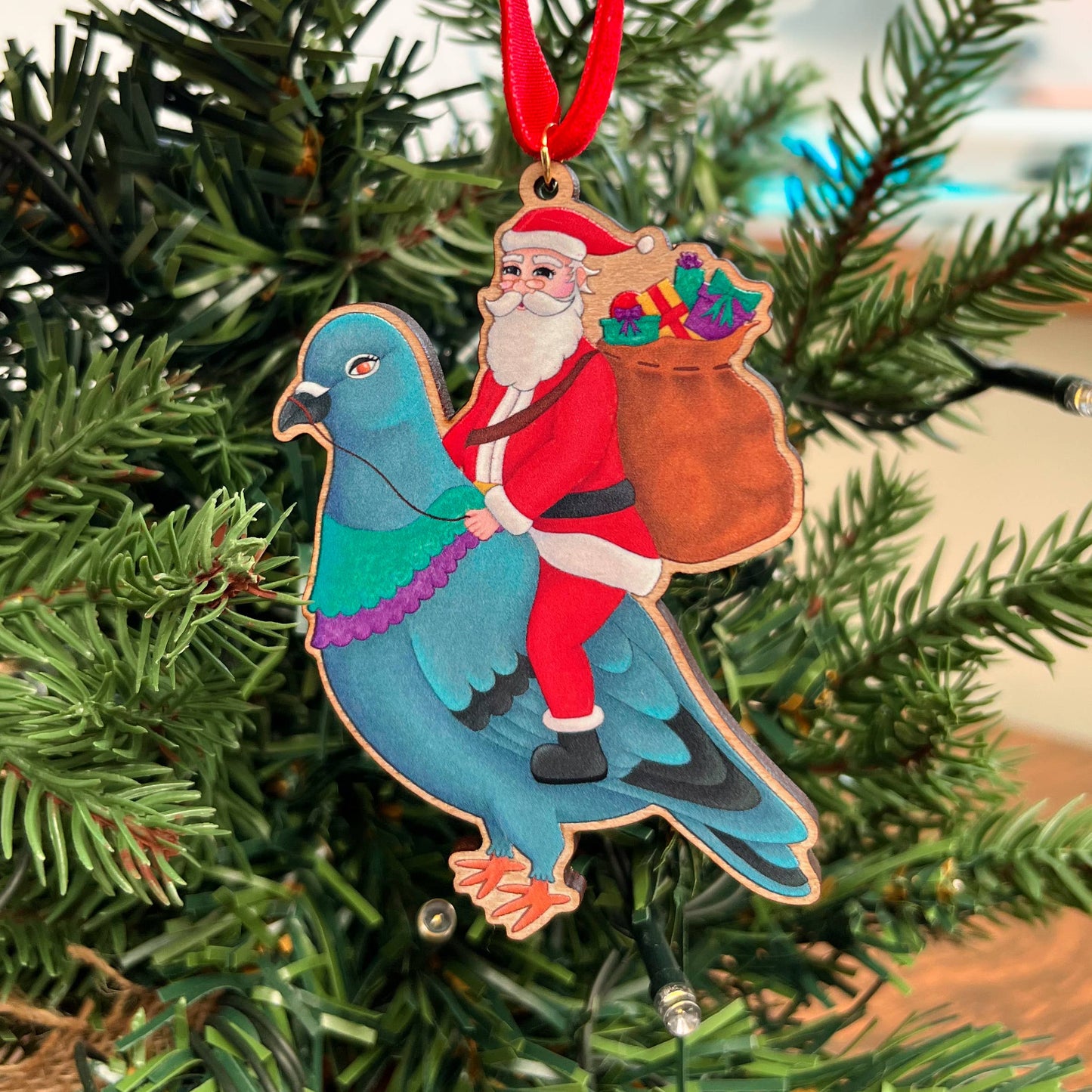 Santa Pigeon wooden Christmas tree decoration with Teddy & Kipling illustration, sustainably certified cherry wood, gold-plated ring, and red velvet ribbon.
