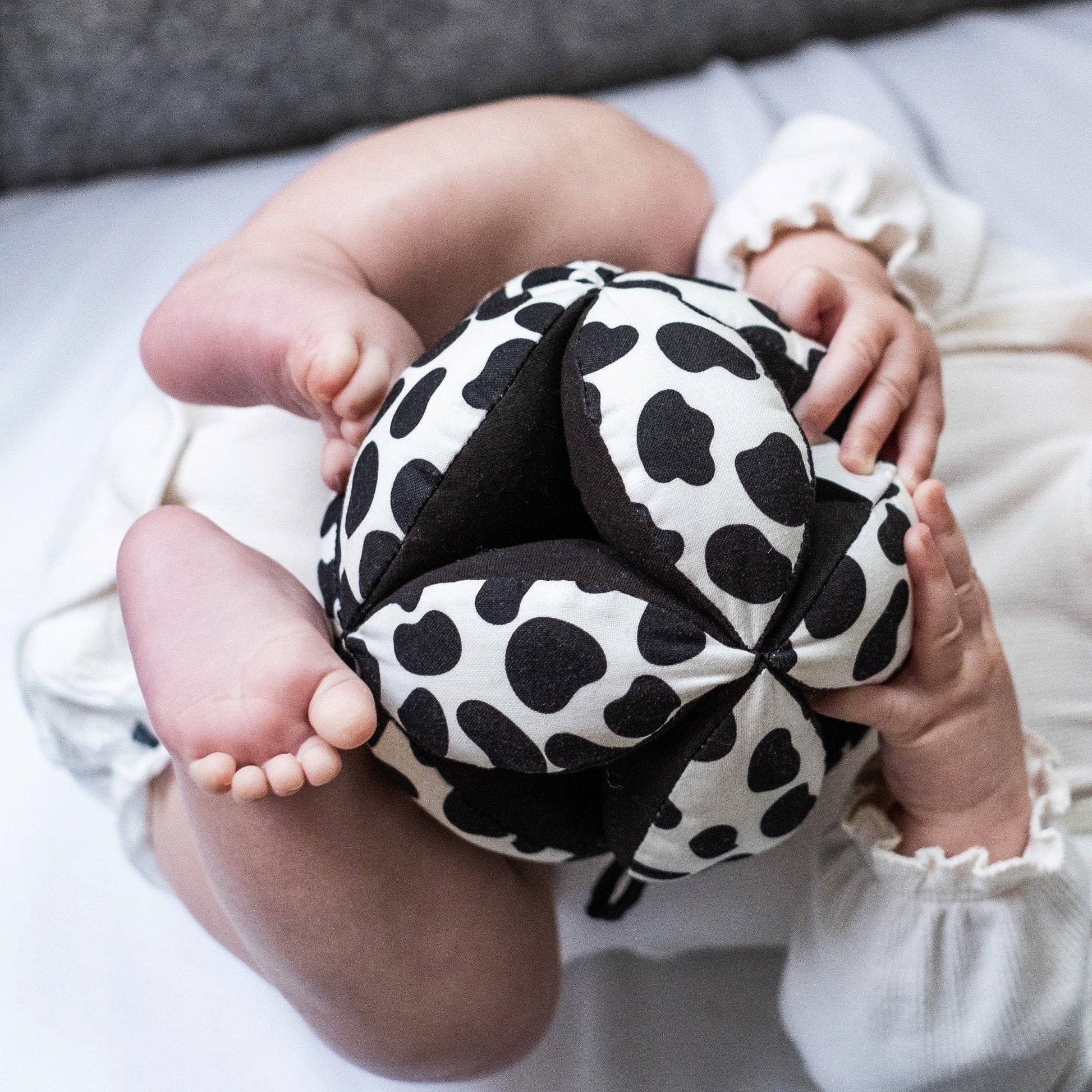Sensory grasp ball in Dalmatian print by Etta Loves, 12cm diameter, made from organic cotton with segments for grasping and a central bell for sensory play.
