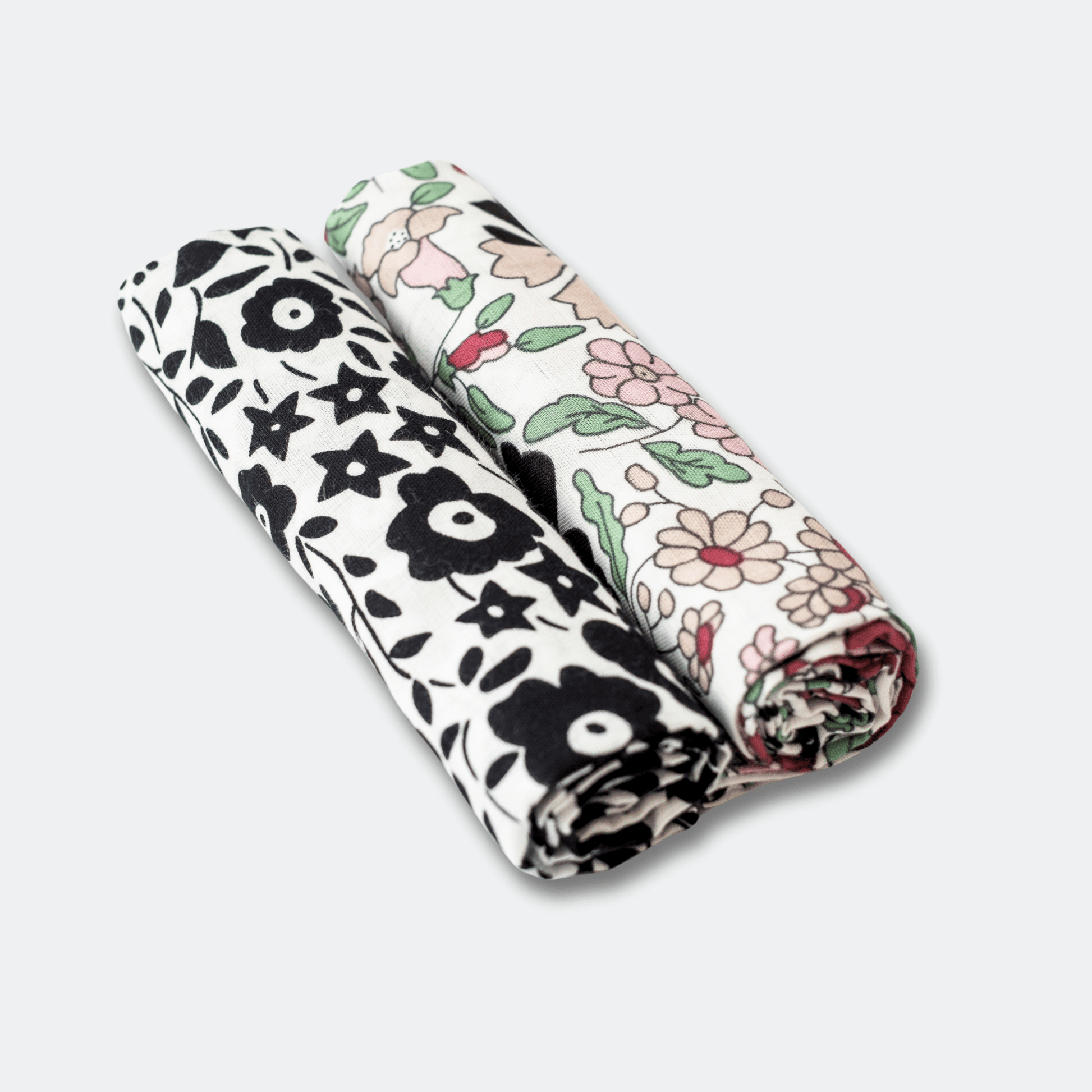 Two folded ETTA Loves Liberty fabric swaddles with black floral and colourful floral patterns on a light grey background.