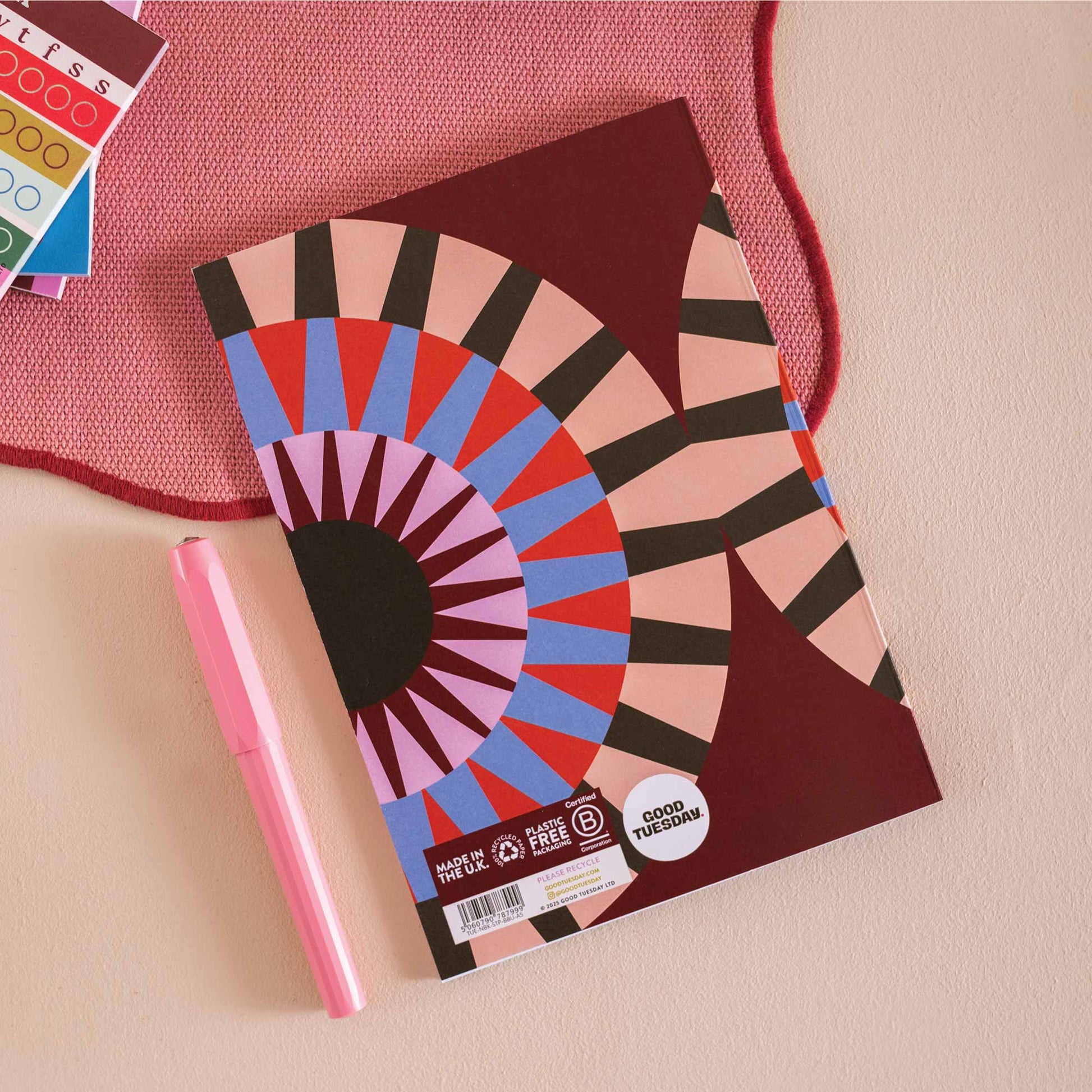 Colourful notebook with geometric design and 'Good Ideas' text, held by a person with a cup of coffee on a pink surface. UK Made. Eco friendly.