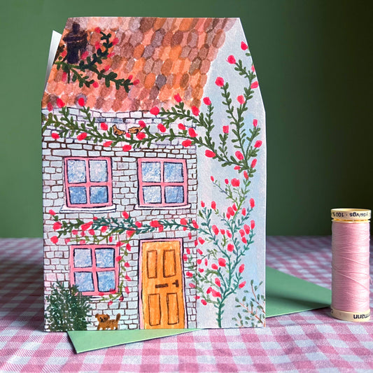 A charming, illustrated blue house with flowers climbing the exterior. The ideal card for celebrating a friend's new home. The card is in the shape of a house.