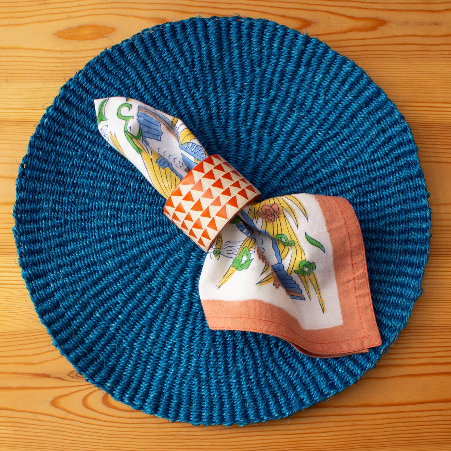 Hand Carved Soapstone Napkin Ring 'Orange Triangles'. Made in Kenya. Shown with an AARVEN Napkin, against a blue placemat.
