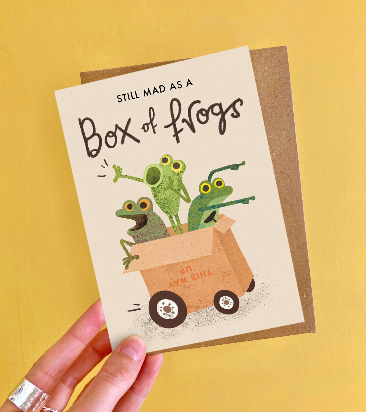 Colourful A6 greeting card featuring whimsical ‘mad as a box of frogs’ illustration by Emily Nash, paired with a recycled kraft envelope.