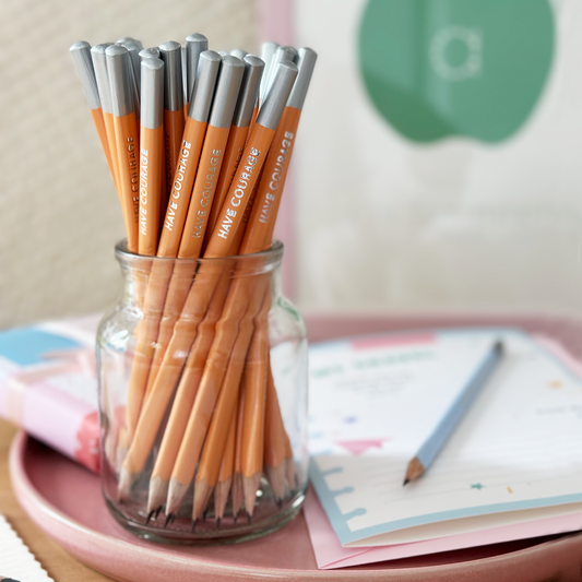 Close-up of orange HB wooden pencil with 'Have Courage' silver foil text and silver tip.