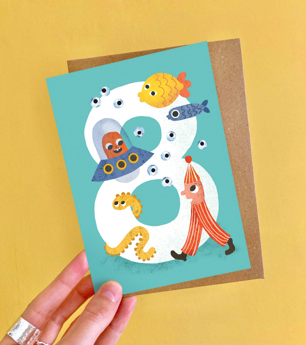 Card with number 8 design featuring cartoon characters and sea creatures on a blue background. By Emily Nash, made in the UK.
