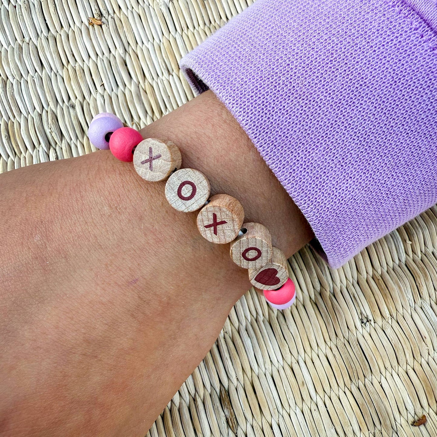Bracelet with wooden beads and pink accents on a wrist against a woven mat background
