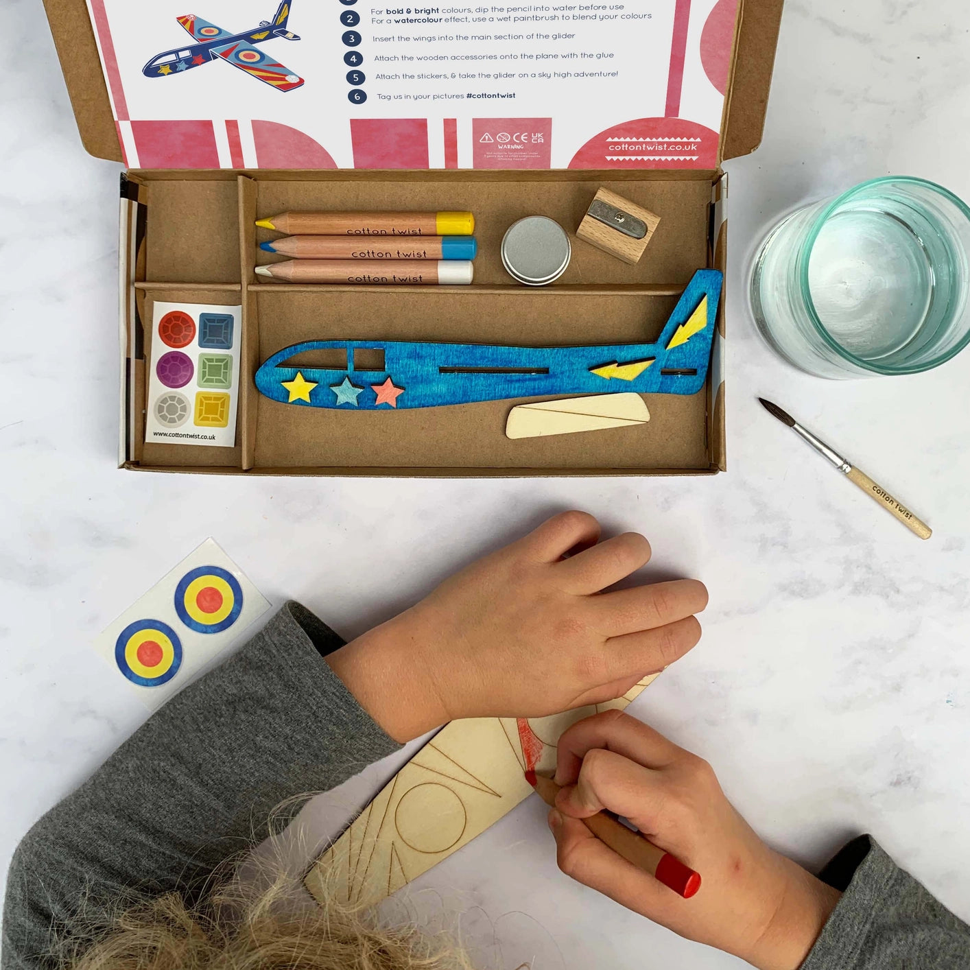 Overhead view of the Cotton Twist Make Your Own Plane Craft Kit laid out with all components: wood, pencils, stickers.