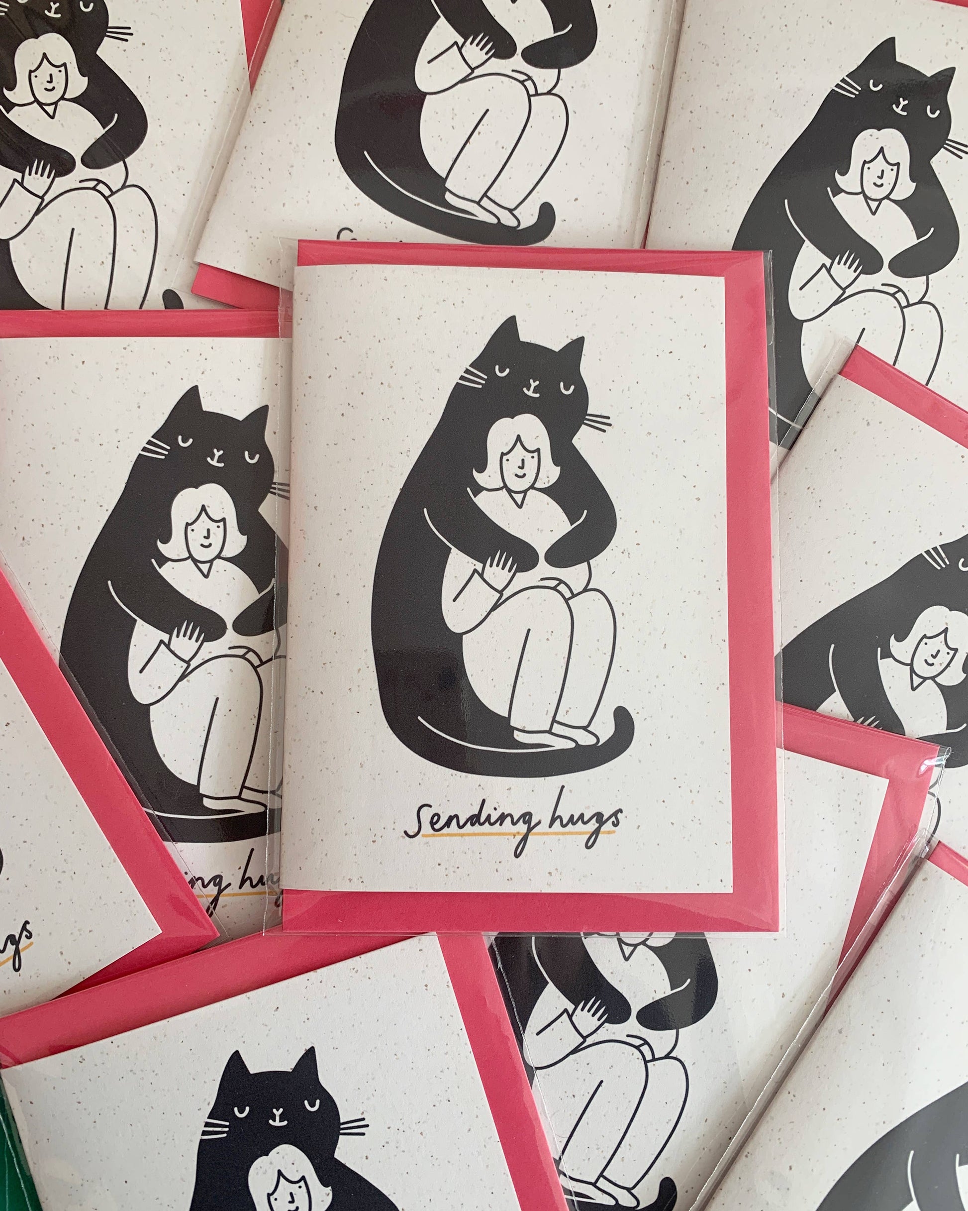 Black and white illustration of a huge black smiling cat cuddling a smaller smiling woman. with the words sending hugs at the bottom of the card.