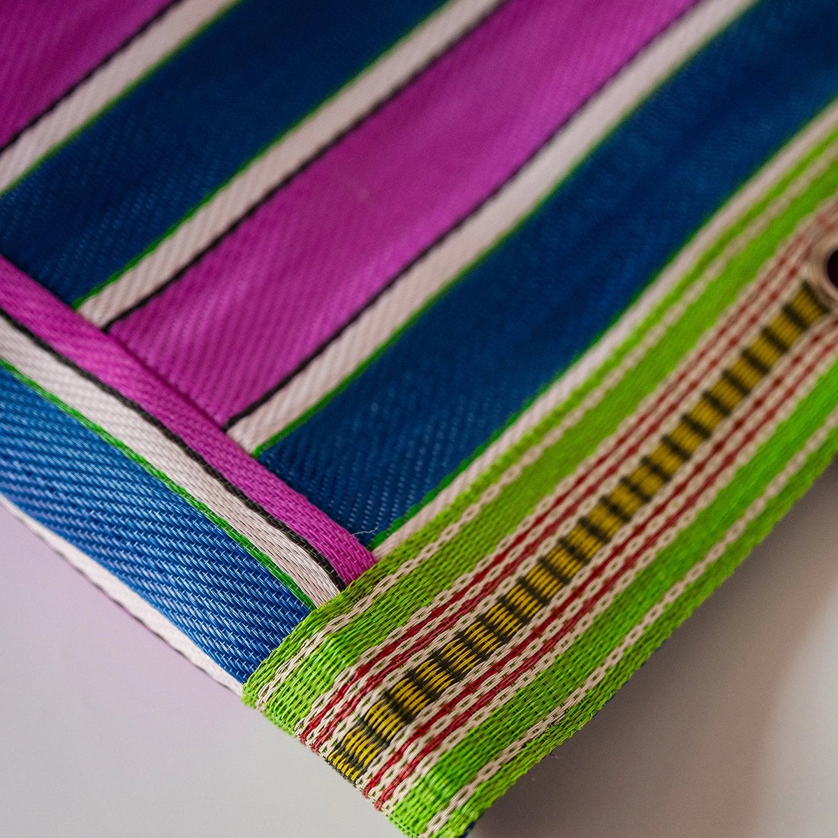 Close-up of a striped woven textile corner, showing bold bands of blue, magenta, white, green, red, and yellow on a light background.