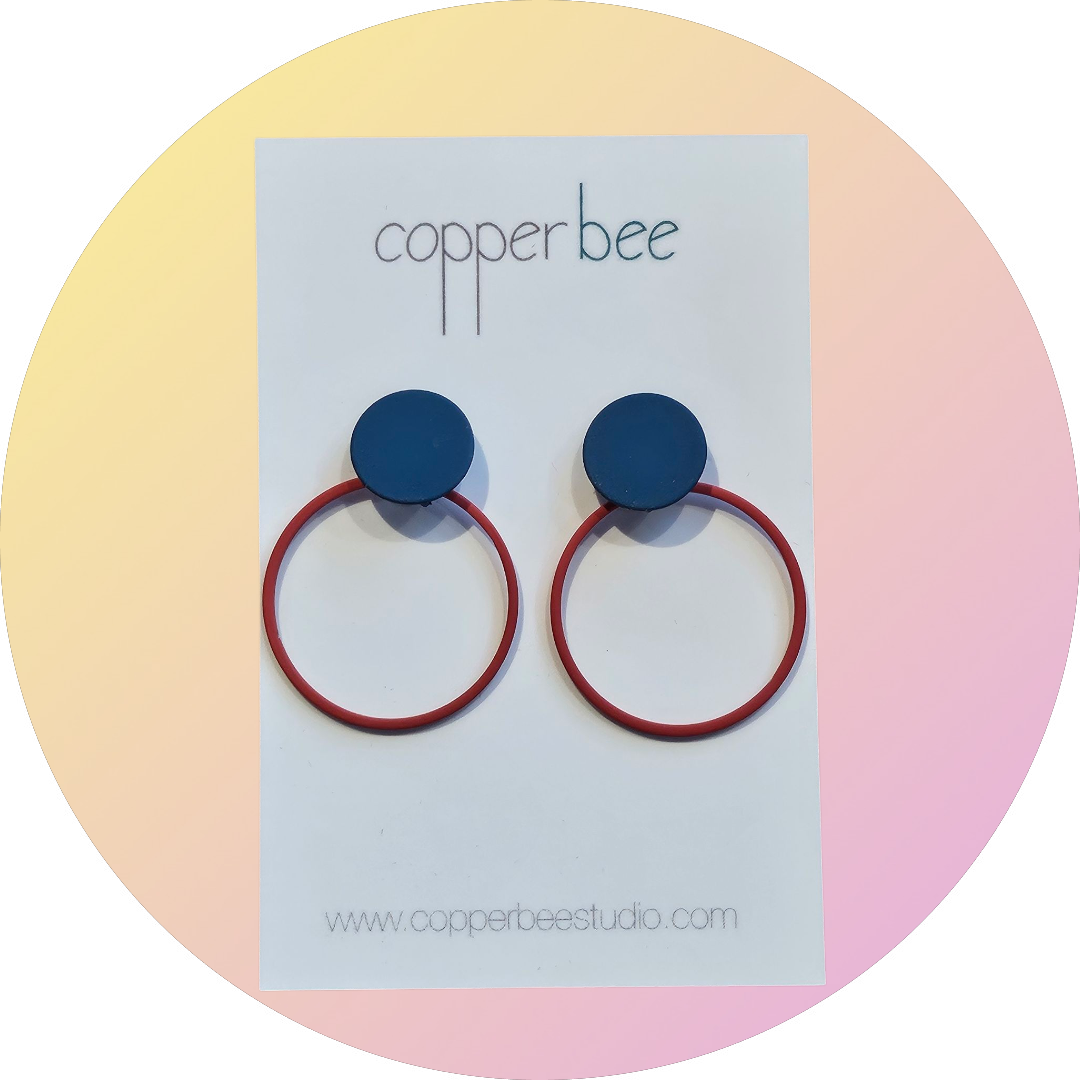 Navy and red earrings on a 'Copper Bee' branded card with a pastel gradient background