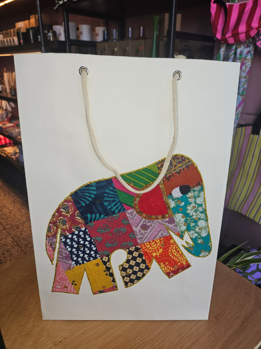 Colourful elephant design on a white gift bag on a wooden surface.