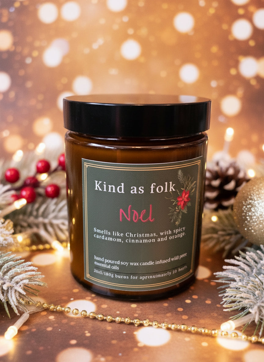 Noel Soy Candle in amber jar with spicy cardamom and orange scent, on a festive green surface