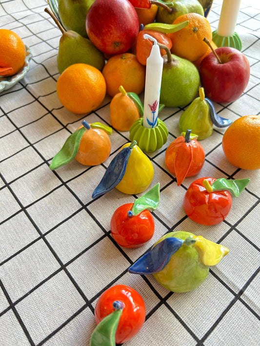 Ruffle & Riot fruit ceramic candle snuffers displayed on a tablecloth alongside larger real fruit, highlighting their miniature size.