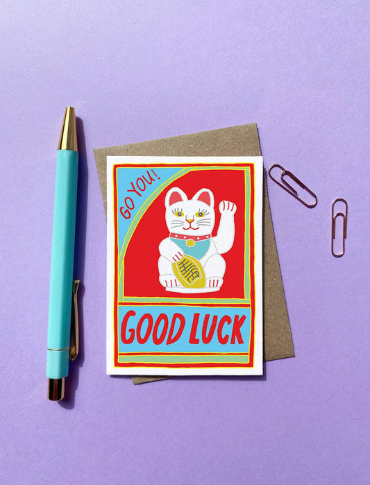 A cute little good luck card featuring a Chinese lucky cat and the words Go You! in the top left hand corner and GOOD LUCK written in bold capitals at the bottom of the card. Illustrated image.